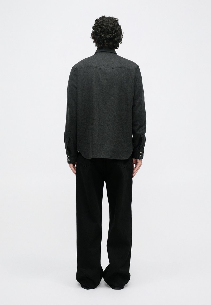 Gray wool shirt with a straight cut, long sleeves, and buttoned cuffs, paired with loose black trousers. Minimalist design, smooth texture.