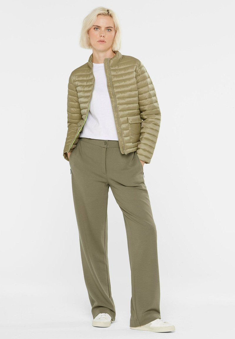 Hellgrüner Pufferjacke mit Reißverschluss vorne und geripptem Kragen, kombiniert mit passenden, lockeren Hosen und weißen Sneakern. Glatte Textur.