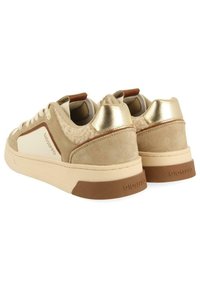 Zapatillas beige con material de ante, detalles en crema, detalles dorados en el talón y panel lateral texturizado. Suela de goma con el logo de la marca en la parte trasera.