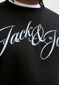 Mustmust, millel on esiotsas suur helesinine kursoriga "Jack & Jones" logo, ribidega kaelus ja pehme tekstuur.