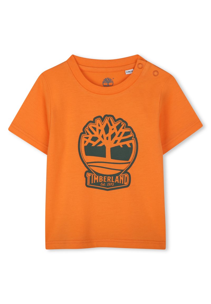 T-shirt in cotone arancione con maniche corte, caratterizzata da un logo Timberland verde scuro e una grafica ad albero. Include un dettaglio con bottoni a pressione sulla spalla.