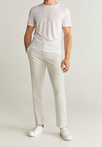 Lichtgrijze, ronde hals t-shirt van een zachte stof, gecombineerd met lichtbeige, slim-fit broek. Witte sneakers maken de look compleet.