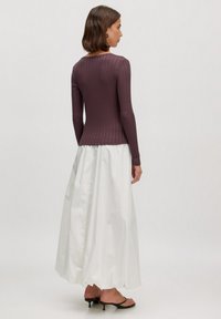 Donkerpaarse geribde langemouwen top gecombineerd met een witte, vloeiende maxirok. De outfit heeft een relaxte pasvorm en minimalistische designelementen.