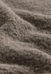 Strukturiertes braunes Gewebe mit weichen, flauschigen Fasern, das eine leicht unregelmäßige Oberfläche und einen dezenten Glanz aufweist, geeignet für Bekleidung oder Heimtextilien.