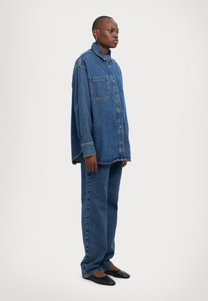 Overdimensjonert denimskjorte med krage, frontlomme og knappelukking, assortert med løstsittende denimbukser, alt i en mellomblå nyanse.
