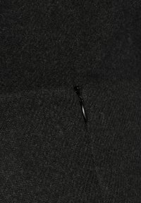 Tissu en laine noir avec une surface texturée et une petite tirette noire se fondant dans le matériau pour un look homogène.
