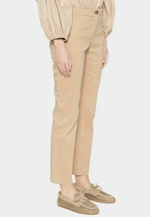 Pantaloni beige a gamba dritta con chiusura con bottoni, indossati con scarpe da barca in rete beige abbinate e una camicetta con maniche lunghe arricciate.