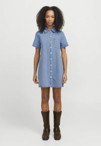 Džinsinė suknelė su trumpomis rankovėmis, apykakle, priekiniu mygtukų užsegimu ir kišenine. Nešiojama su rudais iki kelių batais. Mėlynos spalvos ir vidutinės tekstūros.