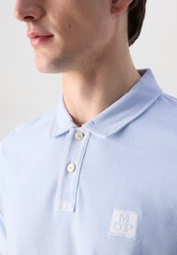 Polo di colore blu chiaro realizzato in tessuto testurizzato, completo di patta con due bottoni, logo ricamato sul petto e un design di colletto classico.