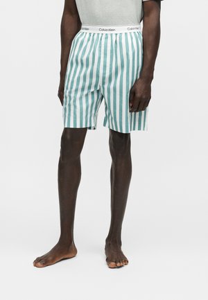Herreshorts til midt på låret med grønne og hvide lodrette striber, elastisk talje med Calvin Klein-logo, båret af en person med mørk hud.
