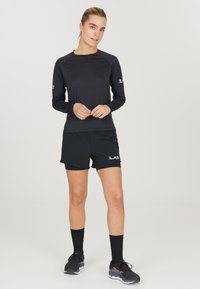 Musta pitkähihainen urh shirt yhdistettynä mustiin shortseihin. Asusteessa on sileä pinta, hienovarainen brändäys ja urheilujalkineet.