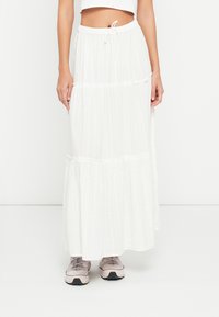 Jupe longue blanche en tissu léger avec un design à volants, dotée d'une taille à cordon et de rayures texturées subtiles.