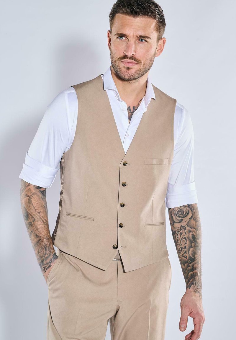 Beige maßgeschneiderte Weste mit Reverskragen, Fünf-Knopf-Verschluss und Taschen, getragen über einem weißen Hemd. Verfügt über eine glatte Textur.