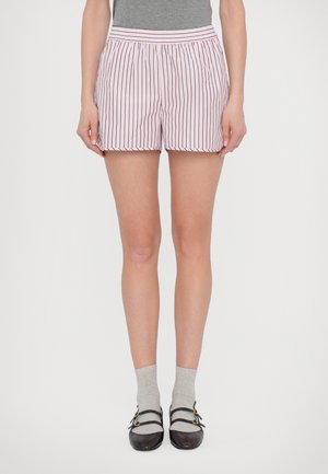 Persona con pantalones cortos a rayas verticales rosas y blancas, calcetines grises hasta la mitad de la pantorrilla, zapatos Mary Jane negros y top gris corto a la altura de la cintura.