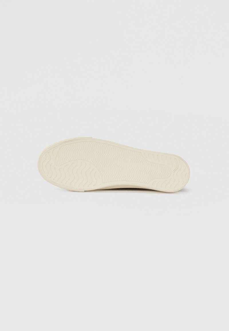 Semelle de chaussure en caoutchouc blanc cassé avec un motif en vagues pour l'adhérence, d'une texture lisse et d'une forme arrondie.