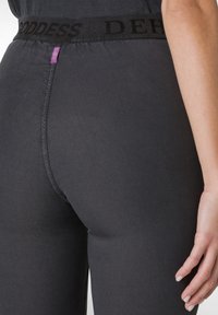 Leggings neri con una ampia vita nera che presenta la scritta "GODDESS" in rilievo. Tessuto liscio con silhouette aderente e dettagli di cucitura minimal.