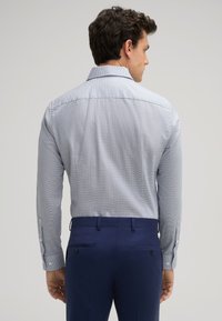 Himmelblaues, mit einem Muster versehenes Hemd mit langen Ärmeln und klassischem Kragen, kombiniert mit dunkelblauen, maßgeschneiderten Hosen mit Gesäßtaschen und Knöpfen.