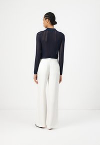 Maglia a maniche lunghe a coste di colore navy con colletto, abbinata a pantaloni bianchi a gamba larga. Entrambi i capi presentano una texture liscia.