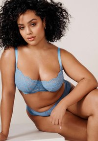 Reggiseno in pizzo blu con slip coordinati, caratterizzato da intricati motivi floreali, spalline regolabili e una morbida texture di tessuto.
