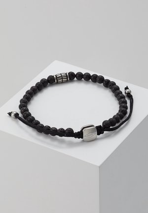 Bracelet noir à perles en pierre de lave, perle décorative en argent et cordon noir réglable avec perles d'extrémité en argent sur une surface blanche.