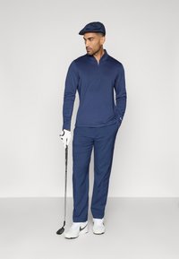 Ναυτικό μπλουζάκι με μακριά μανίκια και μισό φερμουάρ, σε συνδυασμό με ναυτικά παν trousers. Τα αξεσουάρ περιλαμβάνουν ένα καπέλο στο ίδιο χρώμα και μια γκολφ, με λευκά γάντια και παπούτσια.