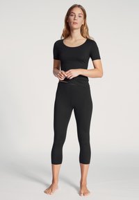 Zwarte top met korte mouwen en driekwart leggings van een zachte, rekbare stof. De outfit heeft een strakke pasvorm en een lichte ronde halslijn.