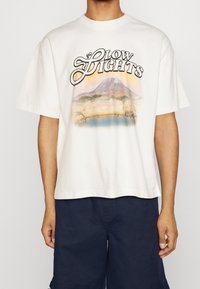 Camiseta blanca de algodón con un gráfico colorido de un paisaje montañoso y el texto "SLOW LIGHTS" encima del diseño. Mangas cortas, corte holgado.