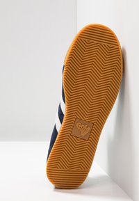 Baskets bleu marine avec rayures blanches, dotées d'une semelle en caoutchouc texturée avec un motif en chevrons et un logo de marque en carré.