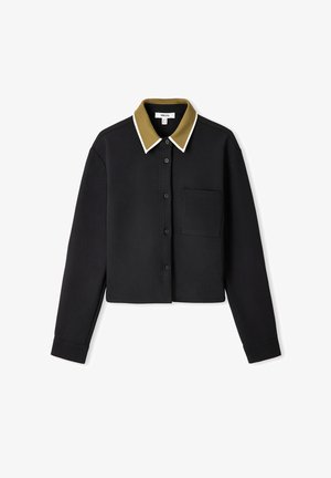 Zwart cropped shirt met lange mouwen, olijfgroene kraag, witte rand, knoopsluiting aan de voorkant en één borstzak. Glad, effen textuur.
