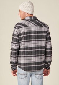 Geruite shirt in zwart, grijs en paarse tinten met een klassieke kraag, lange mouwen en knoopmanchetten; gedragen met een gebreide witte beanie.