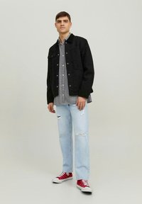 Giacca di jeans nera, camicia a scacchi, jeans strappati azzurri chiari e sneakers rosse. L'outfit ha una vestibilità comoda e uno stile informale.