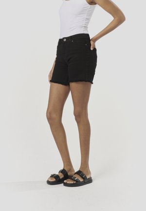 Sorte denimshorts med frynset kant, der har forlommer og lukkes med en enkelt knap. Kombineret med sorte flade sandaler med spænder.