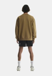 Brun oversized sweatshirt med lange ærmer, ribbede manchetter og kant. Sammen med sorte shorts. Neutral baggrund fremhæver tøjet.