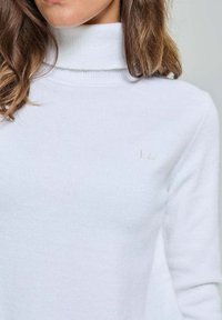 Pull col roulé blanc en tricot doux avec une coupe ajustée et un logo brodé subtil sur la poitrine. Texture lisse et forme élégante.