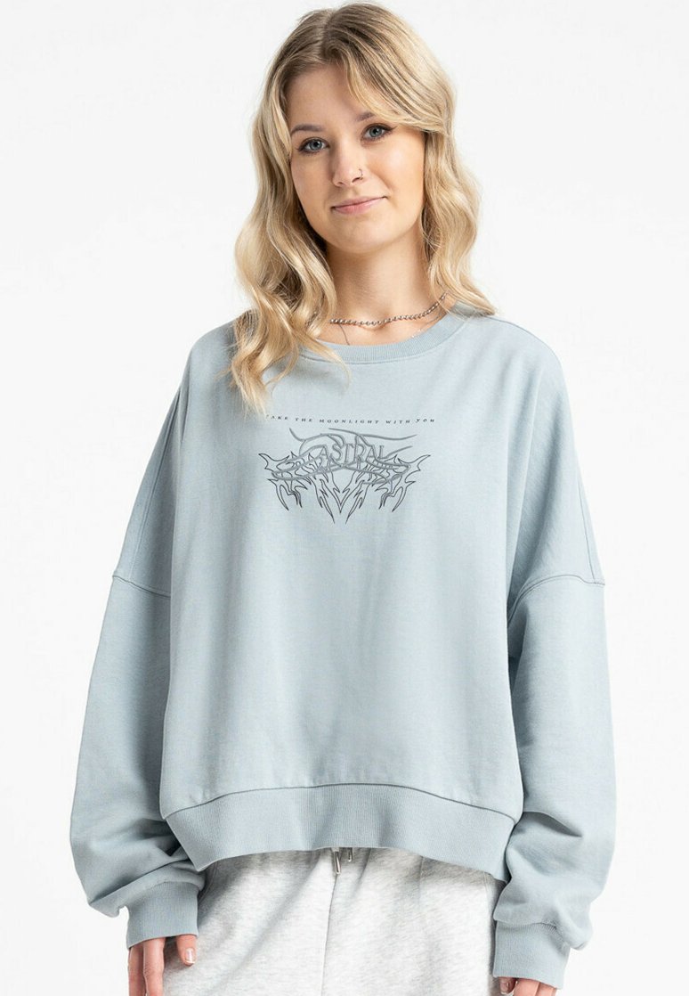 Jasnoniebieski, oversize sweatshirt wykonany z miękkiego materiału. Posiada graficzny nadruk z przodu oraz szerokie, opadające ramiona, co zapewnia luźny krój.