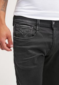 Jeans de mezclilla negra con un corte ajustado, que cuentan con un diseño de cinco bolsillos y un desvanecido sutil. El bolsillo trasero tiene un detalle de logotipo distintivo.