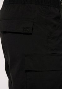 Pantalones cargo negros con una tela texturizada, que cuentan con múltiples bolsillos y una sutil etiqueta de la marca en el lateral. Cintura elástica para mayor comodidad.