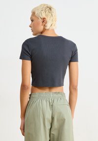 Avskuren, mörkgrå ribbad t-shirt med rund halsringning och korta ärmar, i kombination med ljusgröna byxor med elastisk midja.
