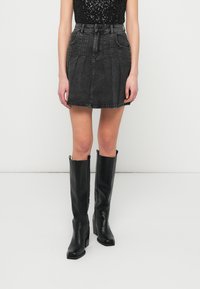 Saia A-line de ganga preta com pregas, complementada por botas altas de couro preto com ponta quadrada e um acabamento brilhante.