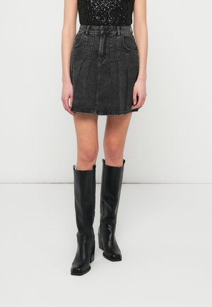 Sort denim A-formet nederdel med plissee, suppleret af høje sorte læderstøvler med firkantet tå og en skinnende finish.