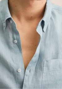 Jasnoniebieska lniana koszula z klasycznym kołnierzykiem, zapięciem na guziki, kieszenią na piersi oraz miękką, teksturowaną powierzchnią.