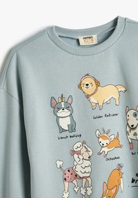 Felpa blu chiaro con grafiche di cani dei cartoni animati, tra cui un Bulldog Francese e un Golden Retriever, con dettagli e colori divertenti.