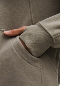 Lys grå sweatshirtstof med ribbet tekstur og manchetter. Har en sidelomme, der understreger et rent, minimalistisk design.