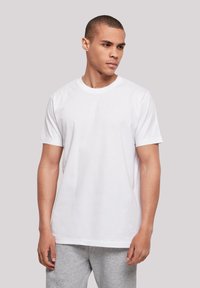 White cotton t-shirt with a crew neckline and short sleeves, worn by a model, paired with gray sweatpants, simple design, smooth texture.