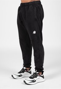 Zwarte sweatpants met elastische tailleband, textuurstof, zijzakken en een wit gorilla logo. Gecombineerd met wit en zwarte sportschoenen.