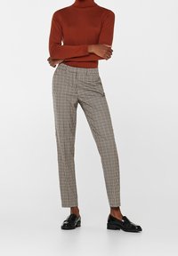 Brun polo-tröja i kombination med rutiga byxor i beige och svart, med slim fit och fickor, bärs med svarta loafers.