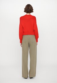 Red knitted sweater with a textured pattern and ribbed hem, paired with wide-fit khaki trousers featuring back pockets.
