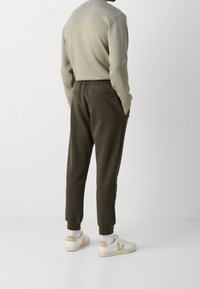 Olivgröna sweatpants med elastisk midja, sidofickor och ribbade manschetter, tillsammans med vita sneakers med beige accenter.