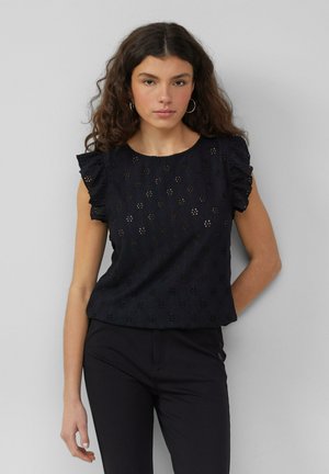 Zwarte geborduurde blouse met korte gerimpelde mouwen, voorzien van bloemen uitsnijdingen en een ronde halslijn. G gedragen met strakke zwarte broek.