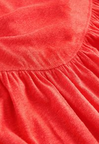 Tissu rouge souple avec des fronces assemblées, créant des volants et de la texture, mettant en valeur les détails et la qualité du matériau.